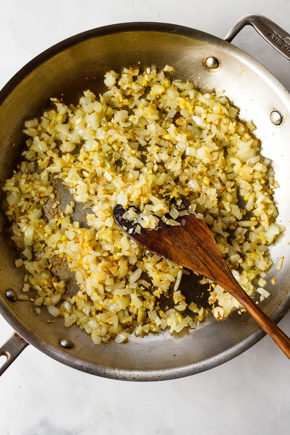 skillet with sautéed onions and wood utensil. 