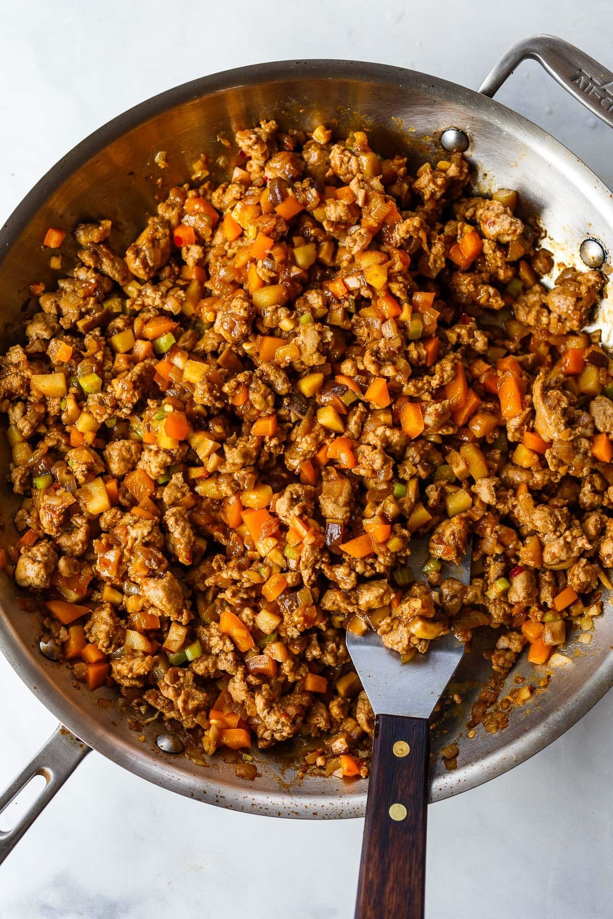 sauté pan with ground meat and veggie filling for Asian lettuce wraps, with spatula. 