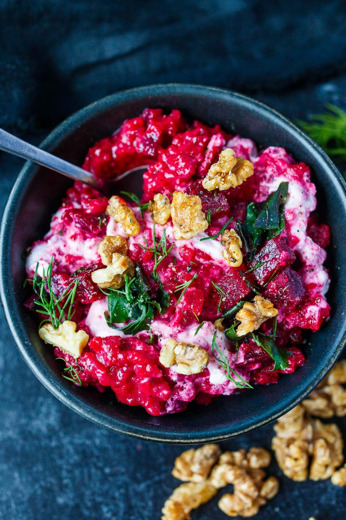 bowl of beet risotto topped with diced beets, walnuts, greens, and dill, with creamy swirl of goat cheese.