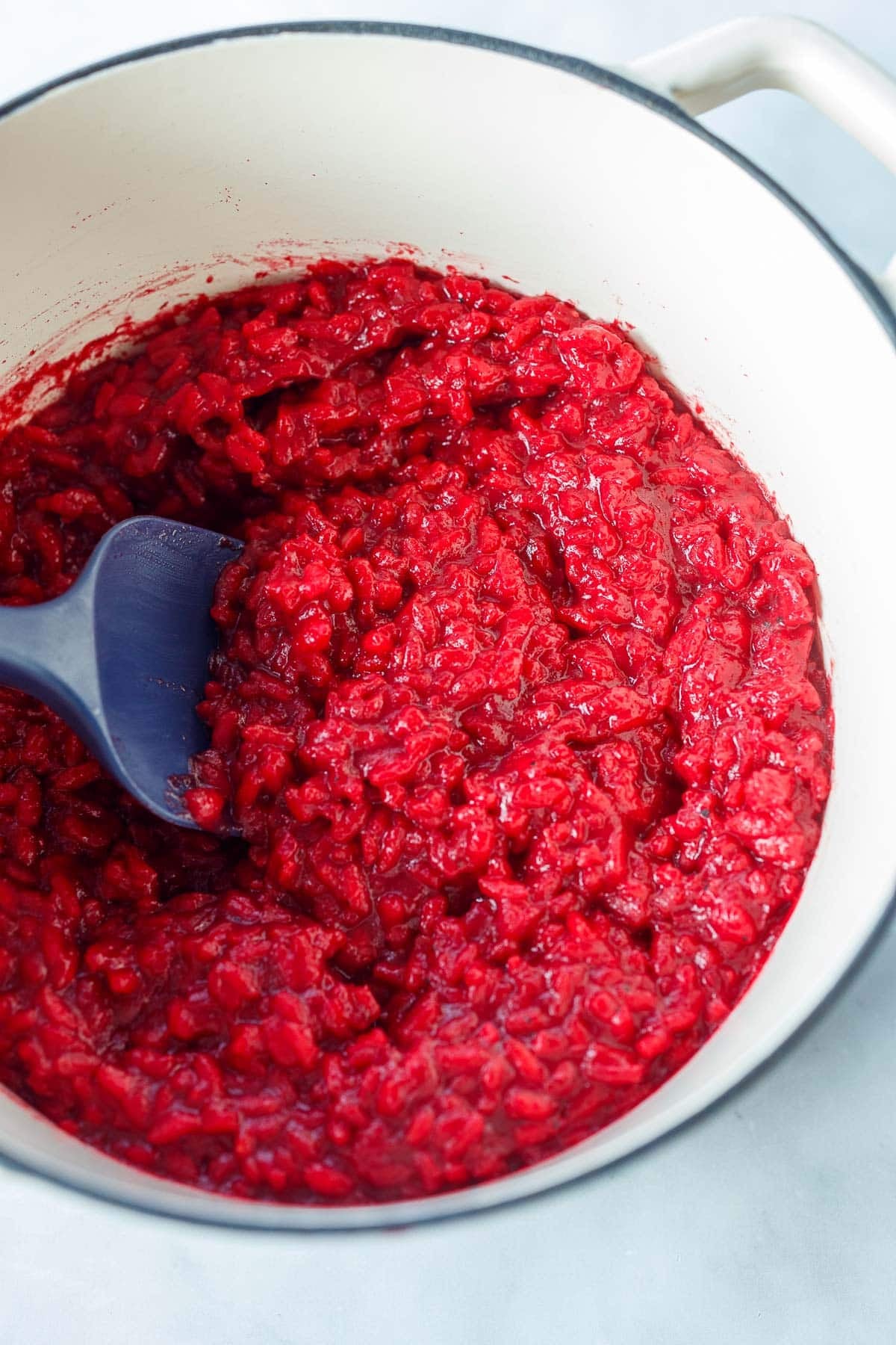 beet risotto in dutch oven with silicone spatula. 