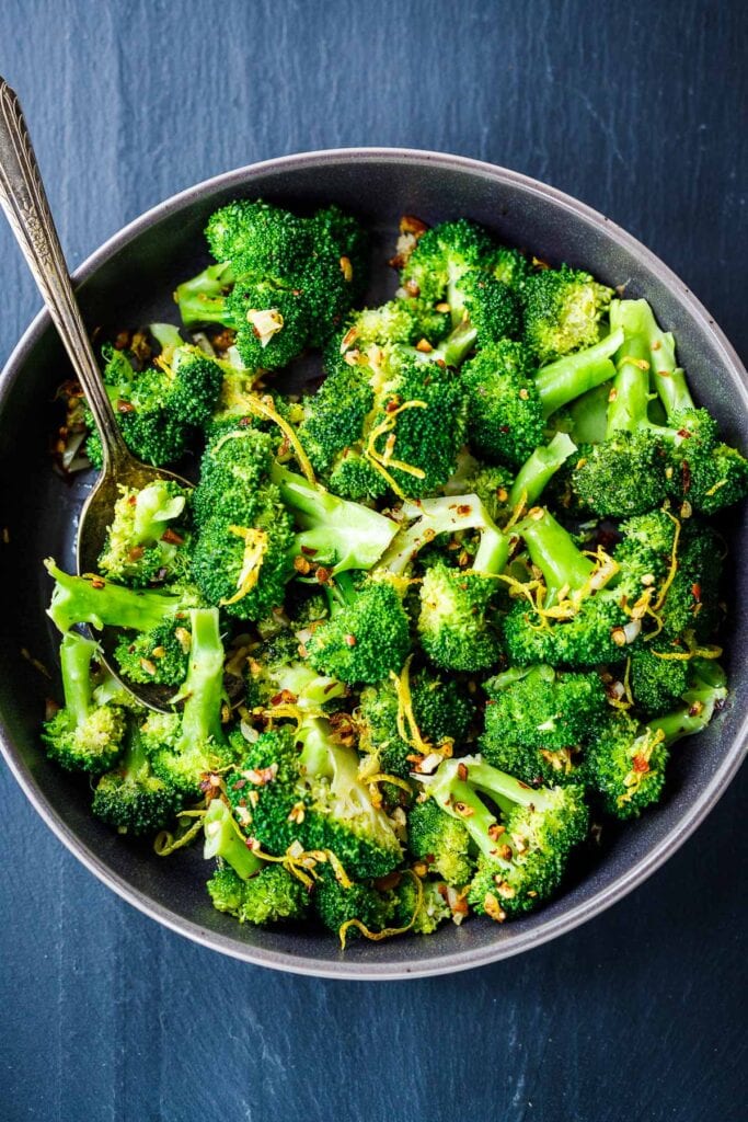 bowl of steamed broccoli garnished with chili flakes and lemon zest.