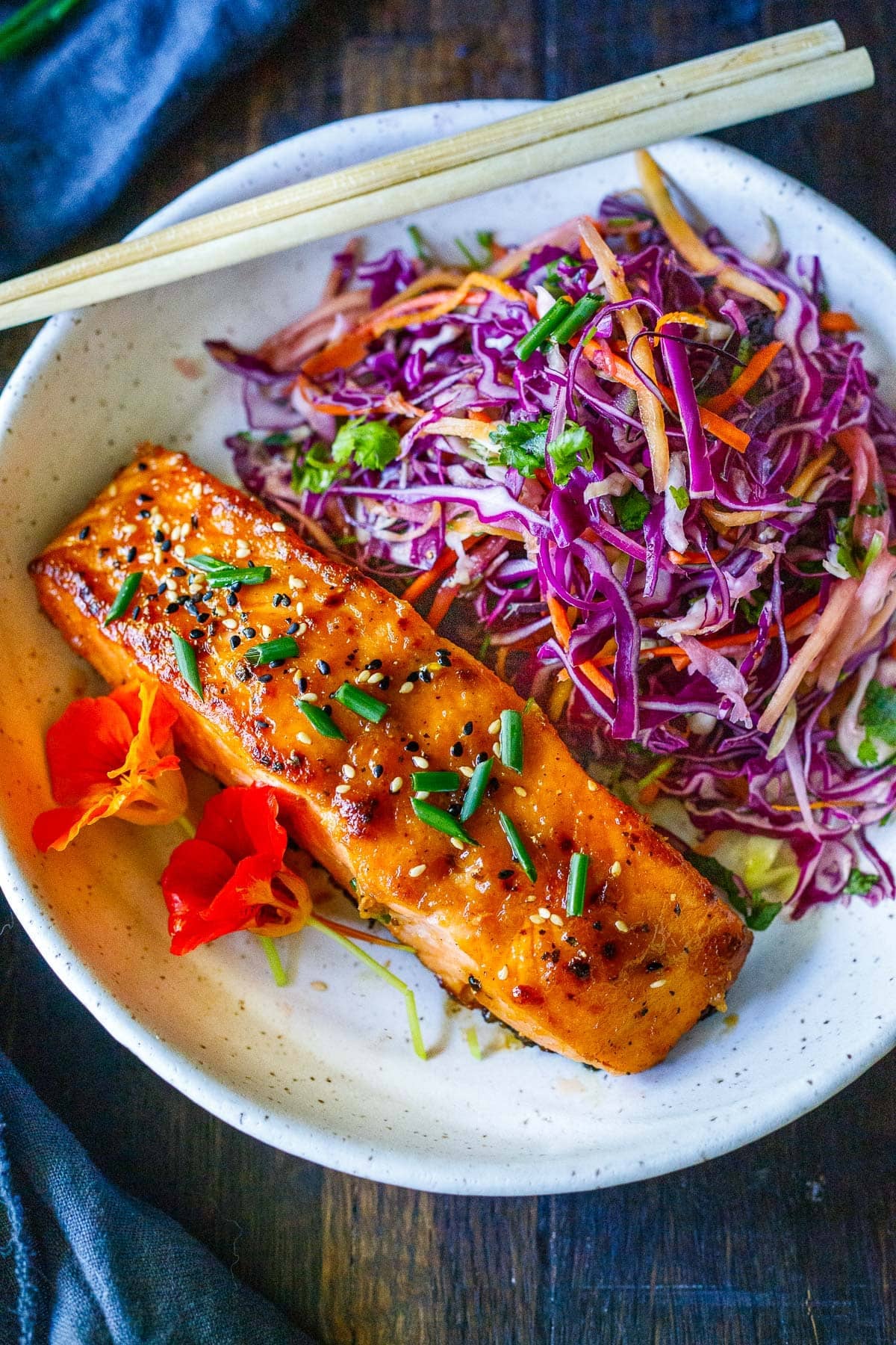 broiled salmon on a plate with Asian slaw and two red flowers.