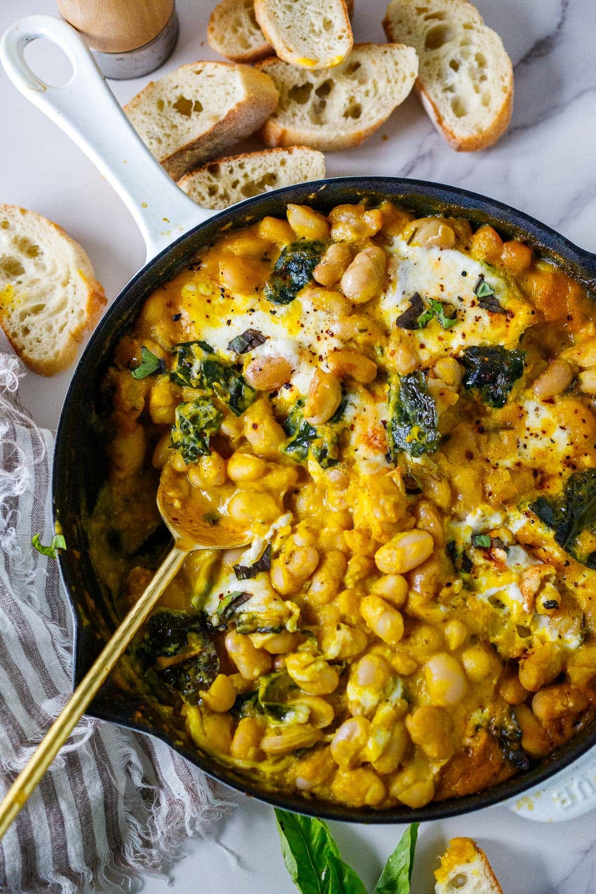butternut baked beans in skillet with burrata cheese, kale, chili flakes, basil, and a spoon.