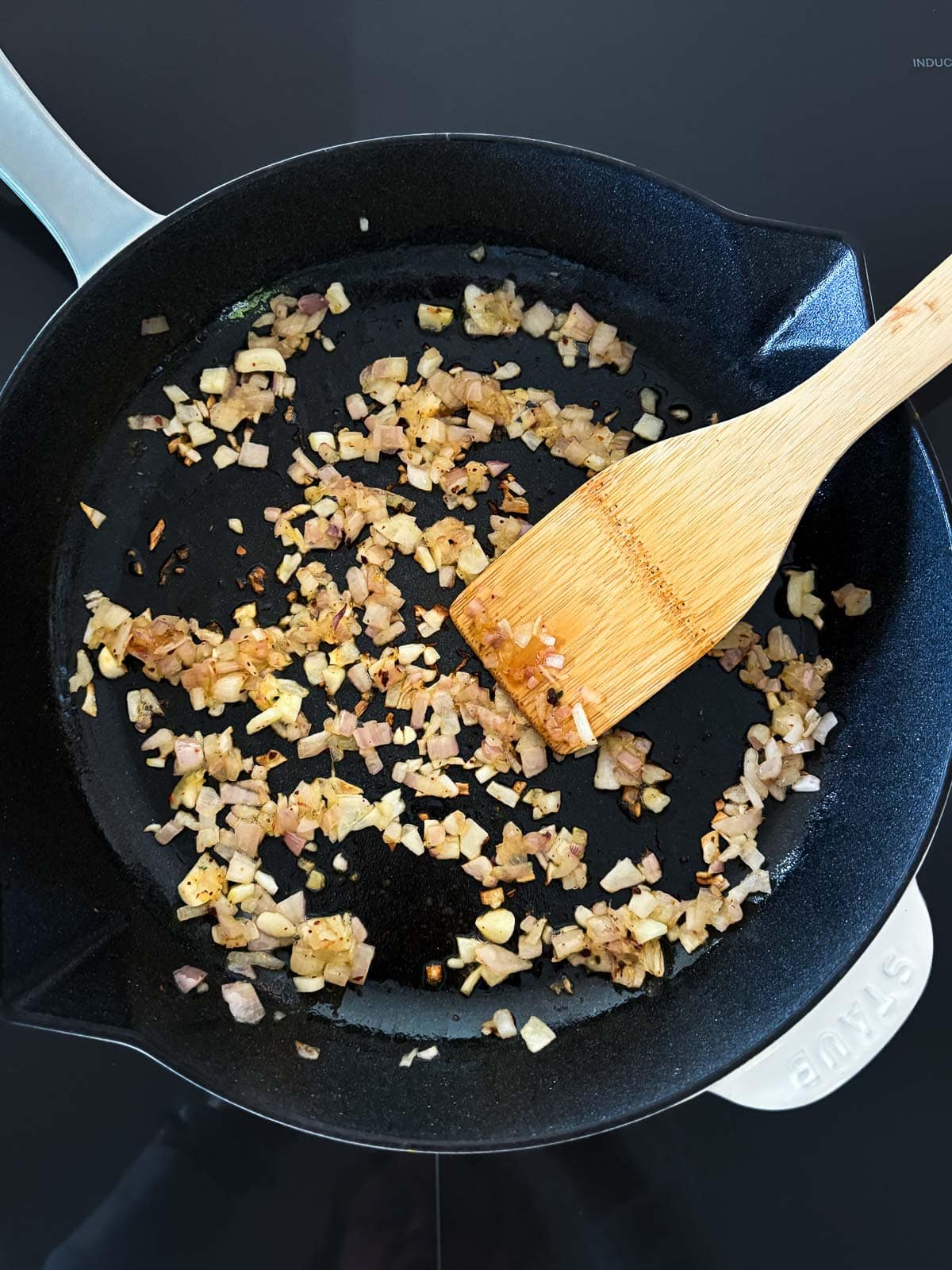 skillet with sautéed garlic and shallots with wood spatula.