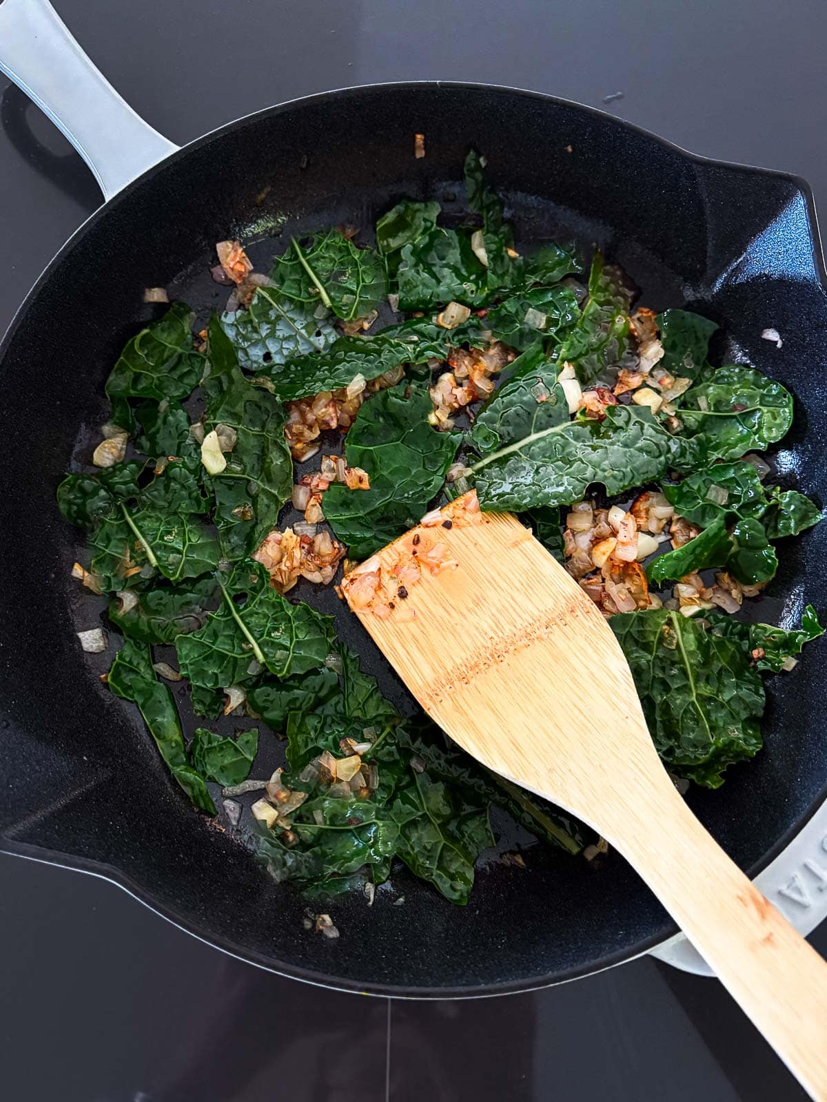 skillet with lacinato kale, sautéed garlic and shallot, and wood spatula.