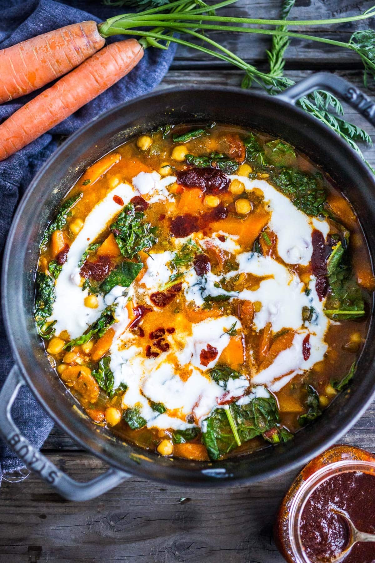 pot of Tunisian chickpea stew with carrots and kale with coconut swirl and harissa paste. 