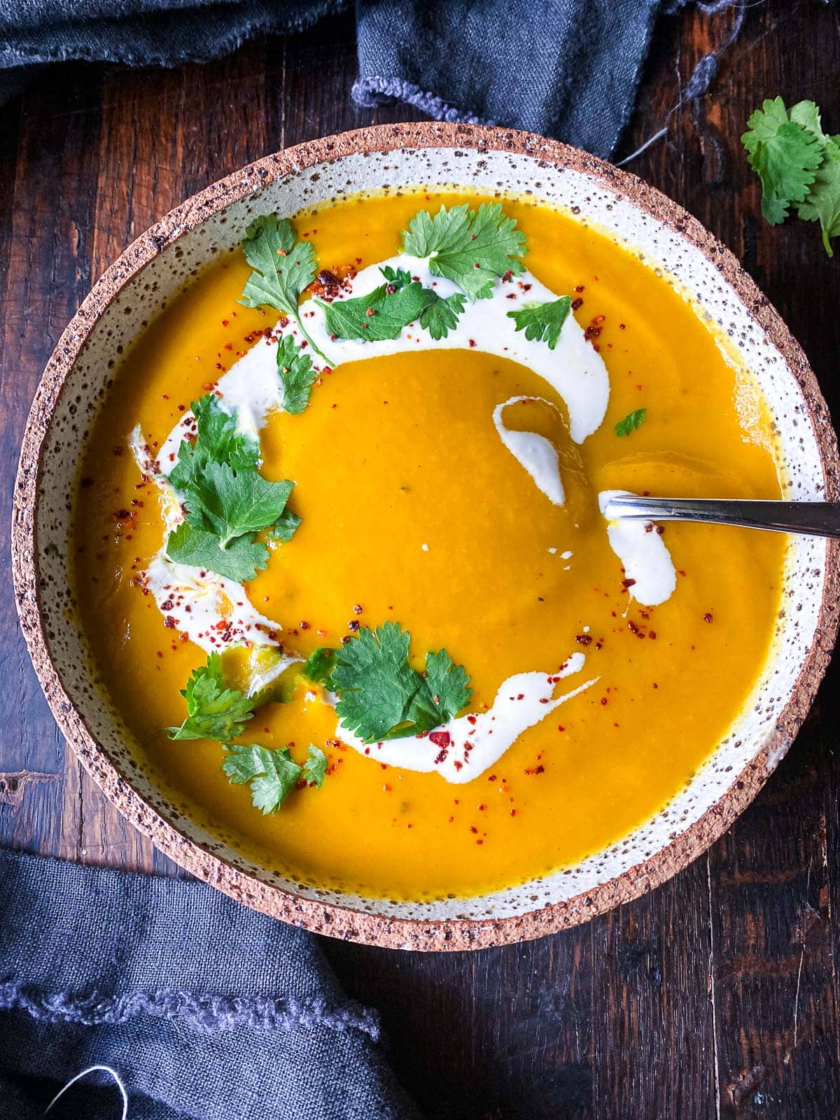 creamy carrot ginger soup in bowl with spoon, swirl of coconut, fresh cilantro, and chili flakes, one of our popular carrot recipes. 