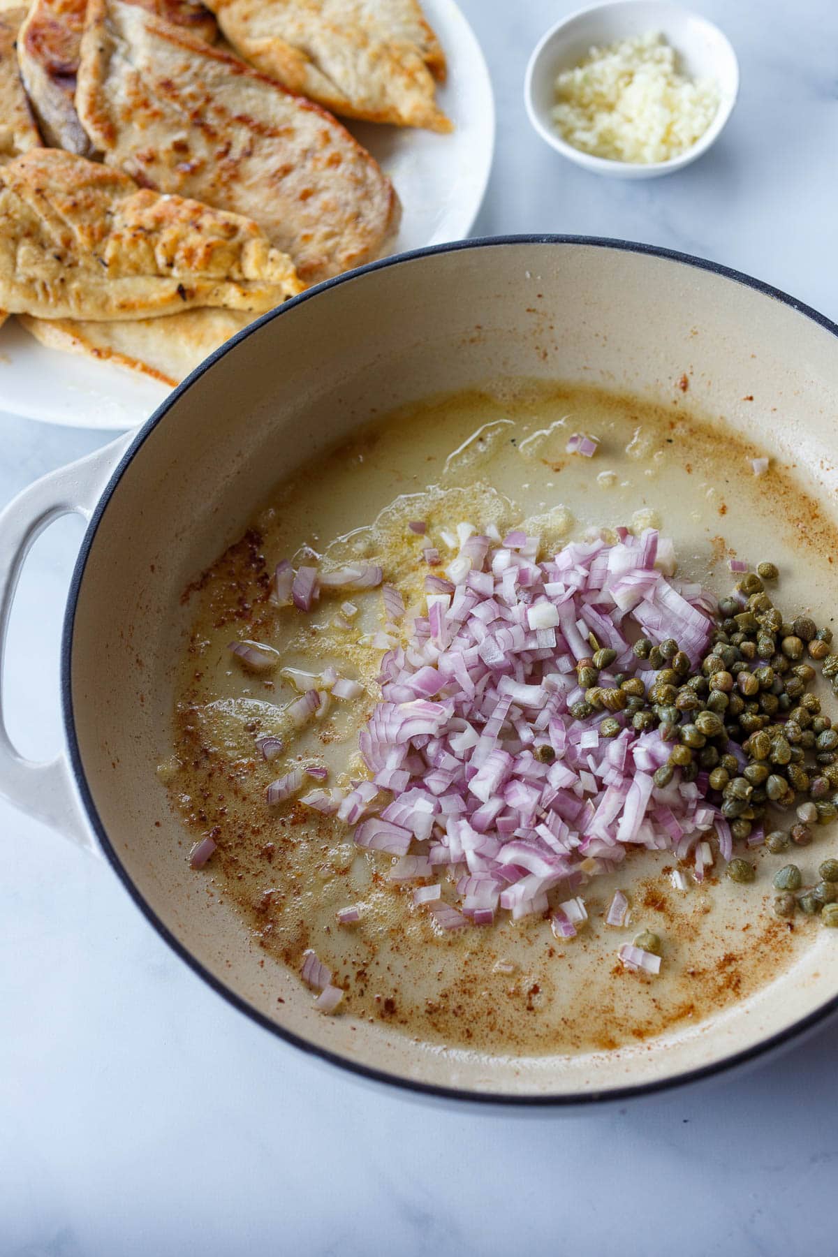 Shallots and capers saut&eacute;ing in pan.