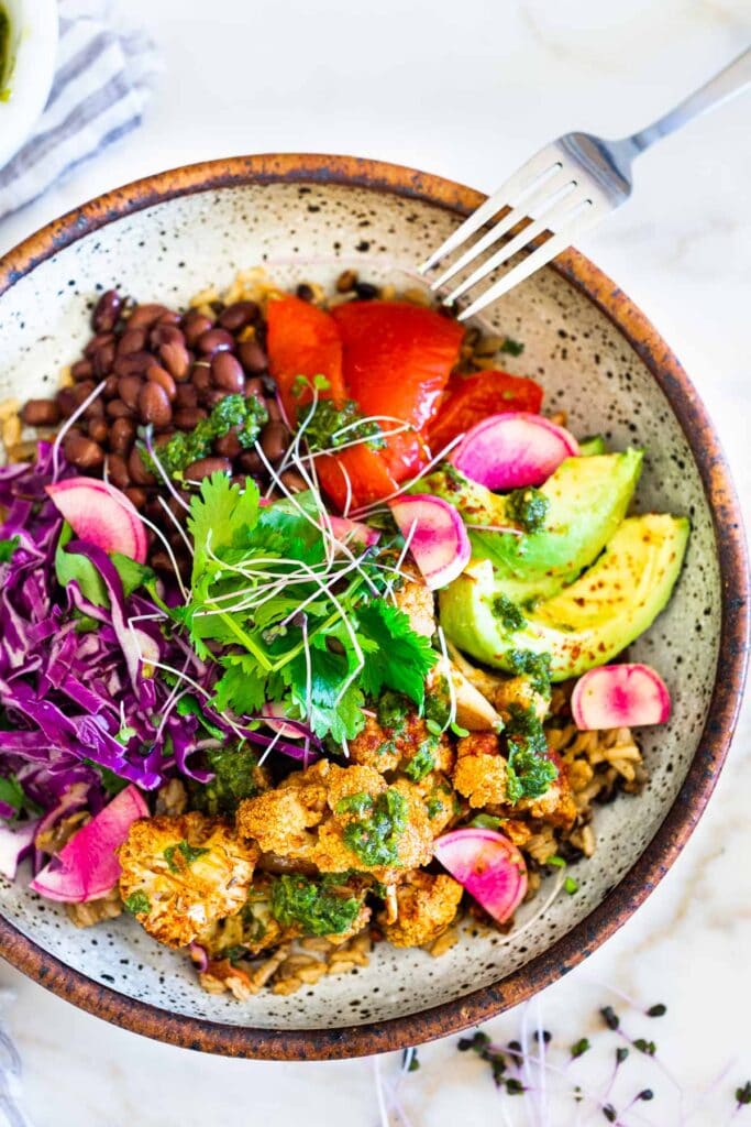 cauliflower chimichurri bowl with black beans, tomato, avocado, radish, cilantro, cabbage, and microgreens.