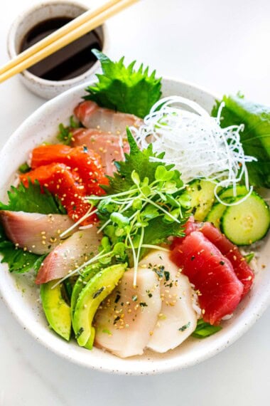 A chirashi sushi bowl with fresh tuna, salmon, avocado, daikon, cucumbers and shiso leaves.