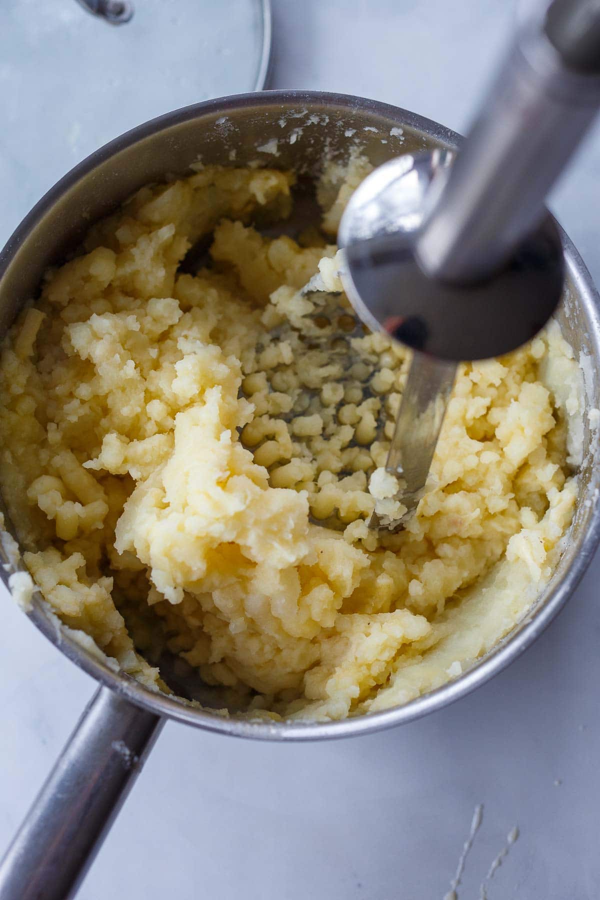 potato masher mashing potatoes in pot.
