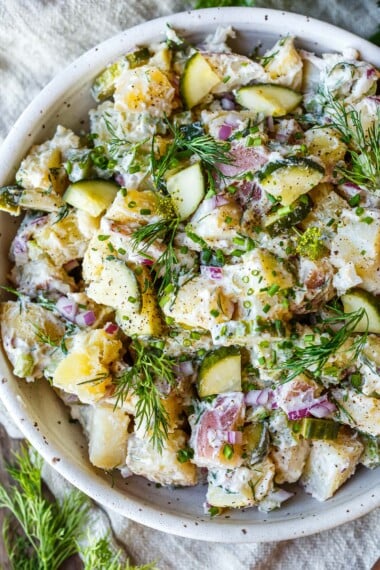 Creamy potato salad with quick pickled cucumbers, fresh dill, and a creamy yogurt dressing, in a white bowl.