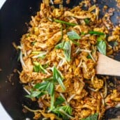 pad thai noodles in wok topped with bean sprouts and fresh herbs with wooden spatula, one of the most popular asian recipes on the blog.