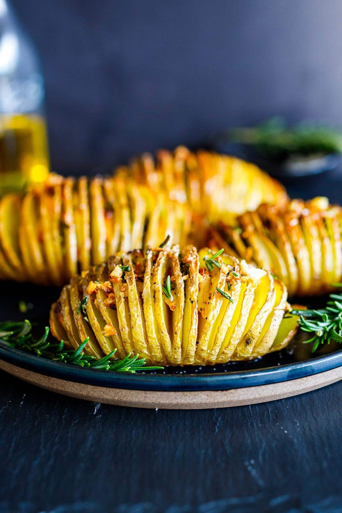 hasselback potatoes with rosemary and garlic on a black plate.