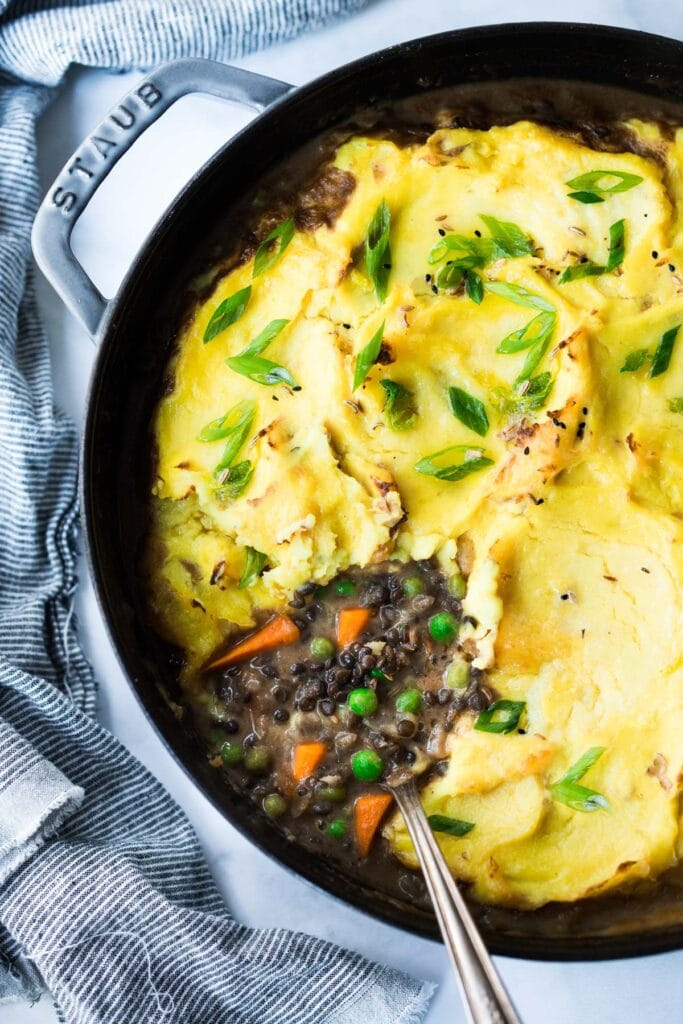 Indian shepherd's pie in cast iron skillet with curried mashed potatoes over lentils, peas, carrots.