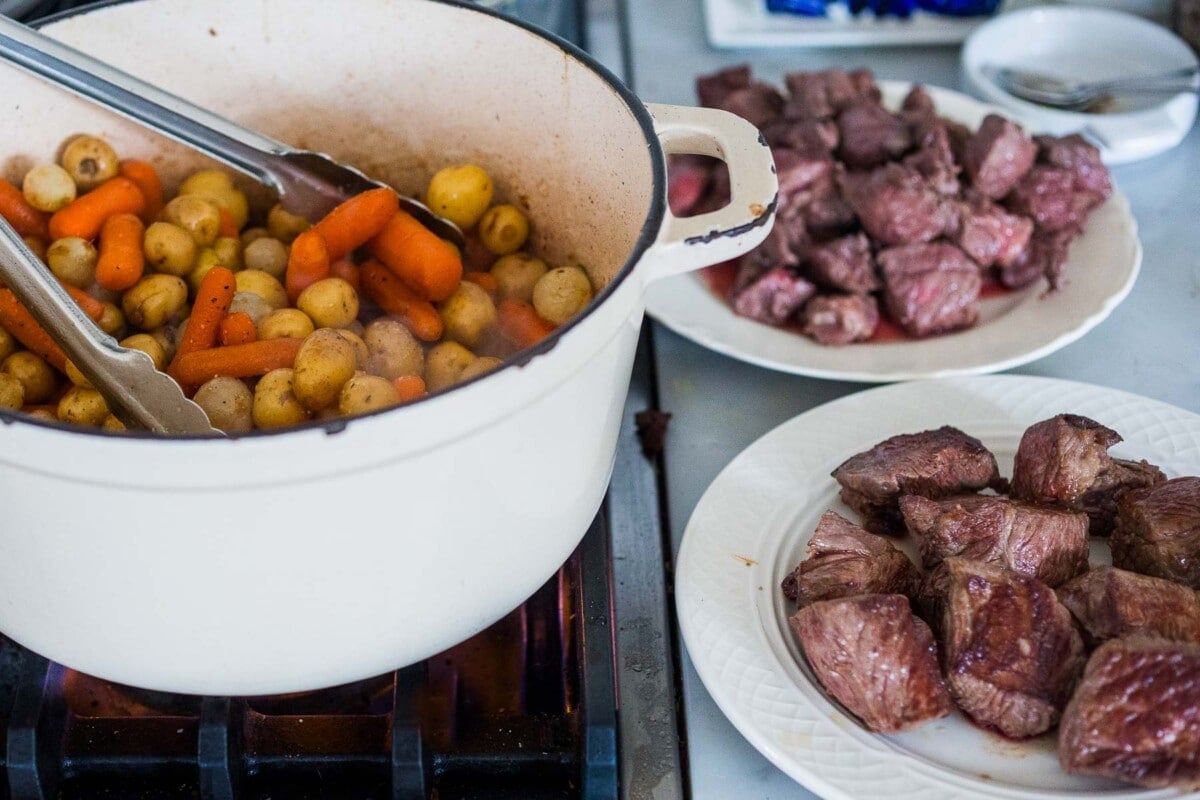 Dutch oven on a stovetop with browned lamb on a plate beside it.