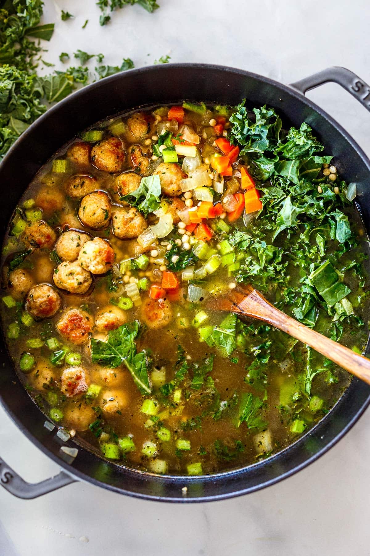 Dutch oven with Italian wedding soup with seared meatballs, onions, carrots, kale, and broth. 