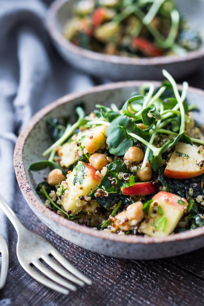 Winter happiness salad in a bowl with quinoa, kale, apples, chickpeas, and sprouts.