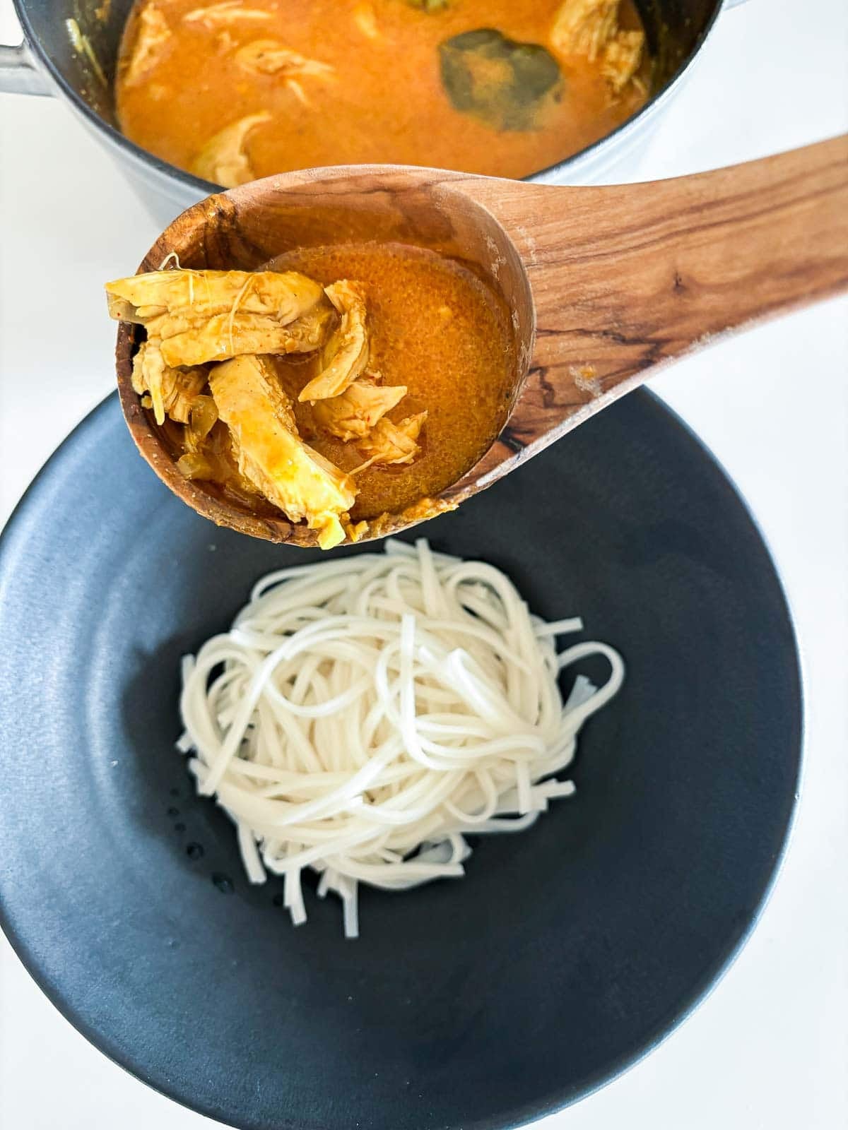 Ladling the khao soi over the noodles in a bowl.