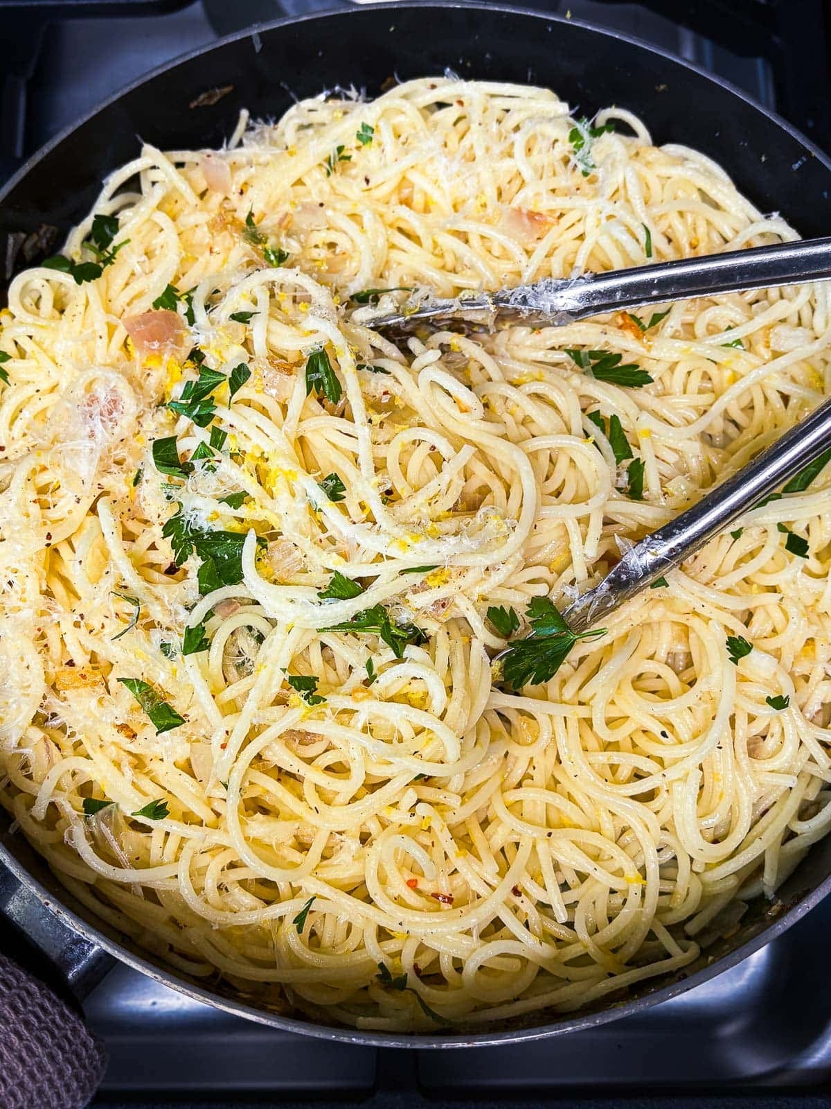 large skillet with lemon pasta with parsley, pecorino stirred in using tongs.