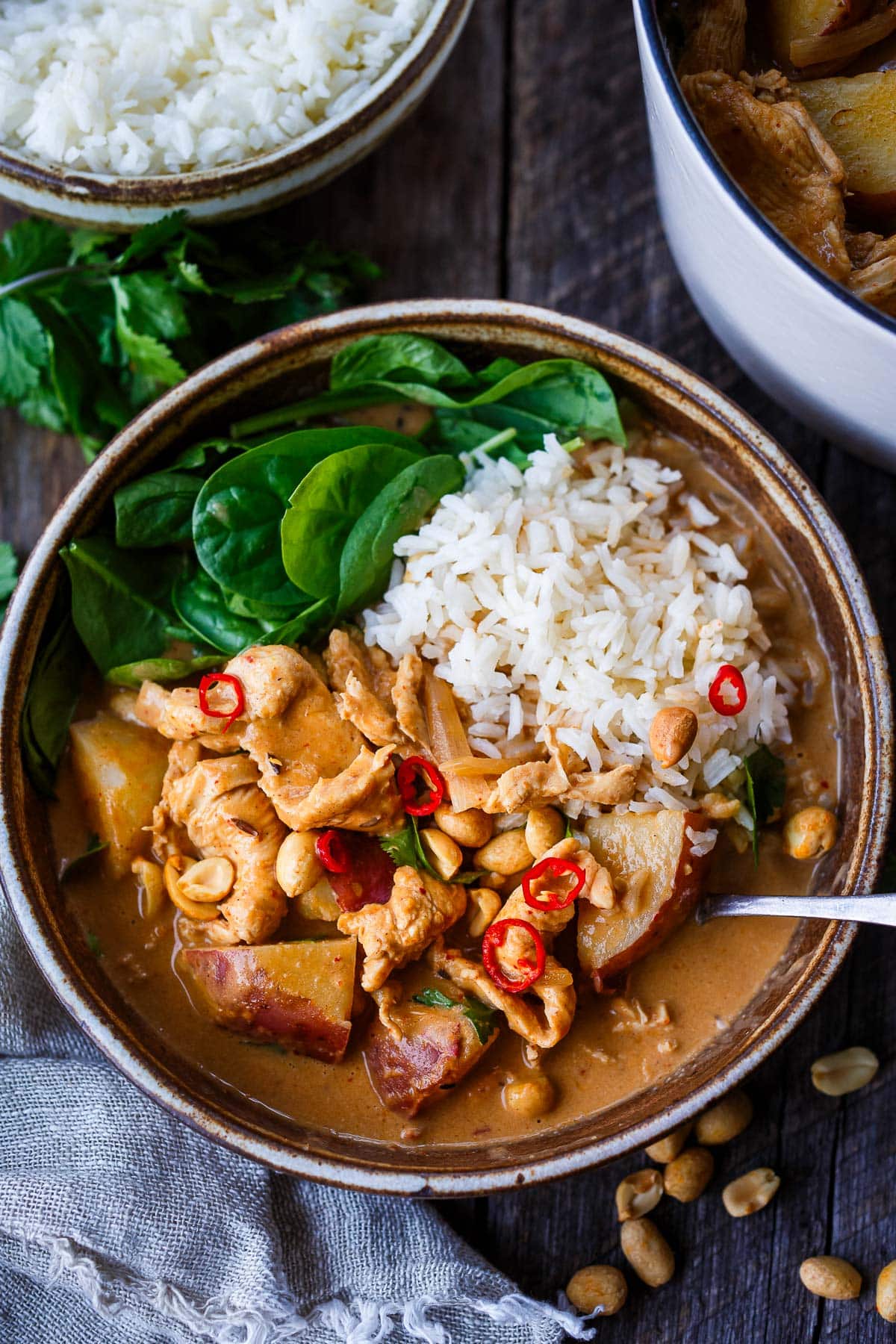 bowl with Thai Massaman Curry with jasmine rice, baby spinach, red chilies, and peanuts.