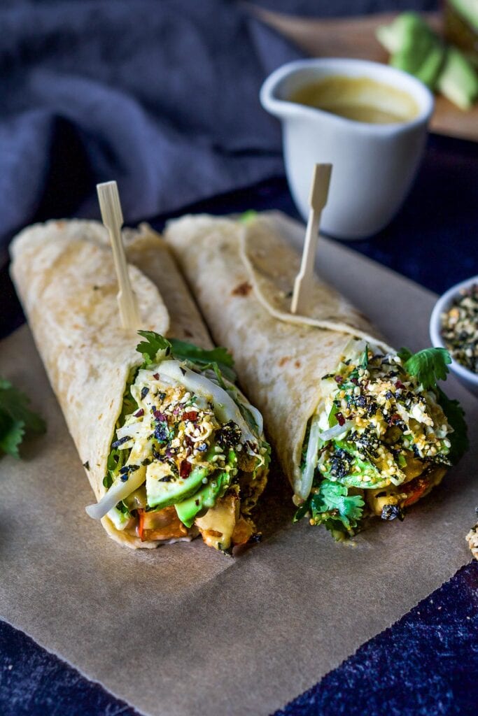 two miso tofu wraps with avocado, herbs, crunchy veggies, and furikake, closed with toothpicks.