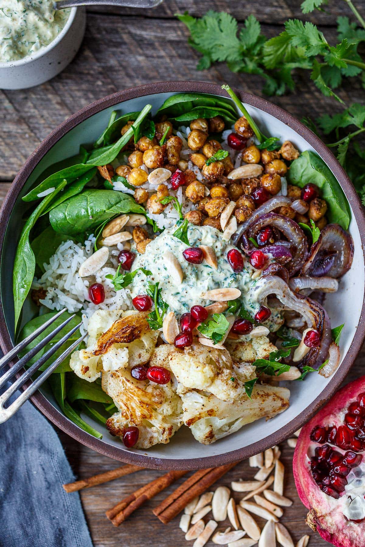 Moroccan cauliflower chickpea bowl with caramelized onion, almonds, pomegranate seeds with sauce over basmati rice and fresh spinach.