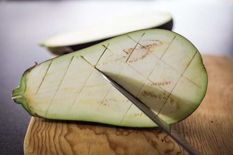 knife scoring eggplant half in crosshatch pattern. 
