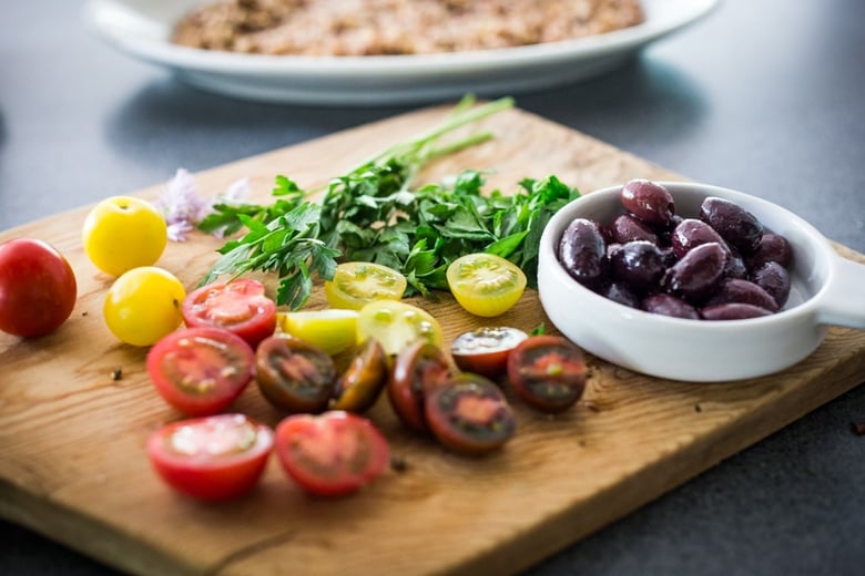 wood board with fresh parsley, cherry tomatoes, and small dish with Greek olives. 
