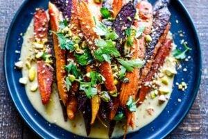 A quick and easy recipe for Roasted Carrots with cumin and coriander seeds, over a creamy Maple-Tahini Sauce, sprinkled with Pistachios and Dukkha, a tasty vegan side dish that pairs with many things. 