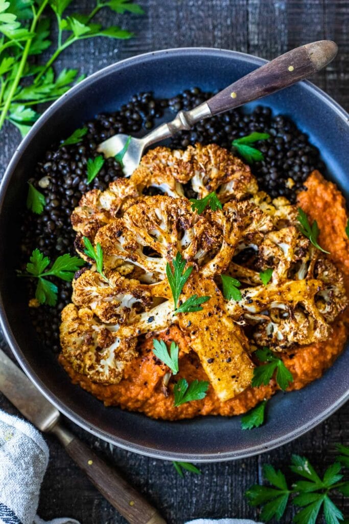 roasted cauliflower steak on romesco sauce with braised lentils, garnished with parsley.