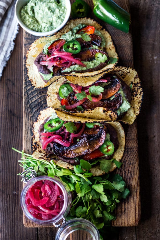 wood board with chipotle portobello mushroom tacos topped with pickled onions, jalapeno, and cilantro.