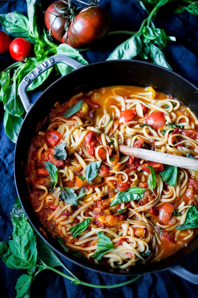 large pan with spaghetti with fresh tomato sauce topped with basil with wood spoon stirring the pan.