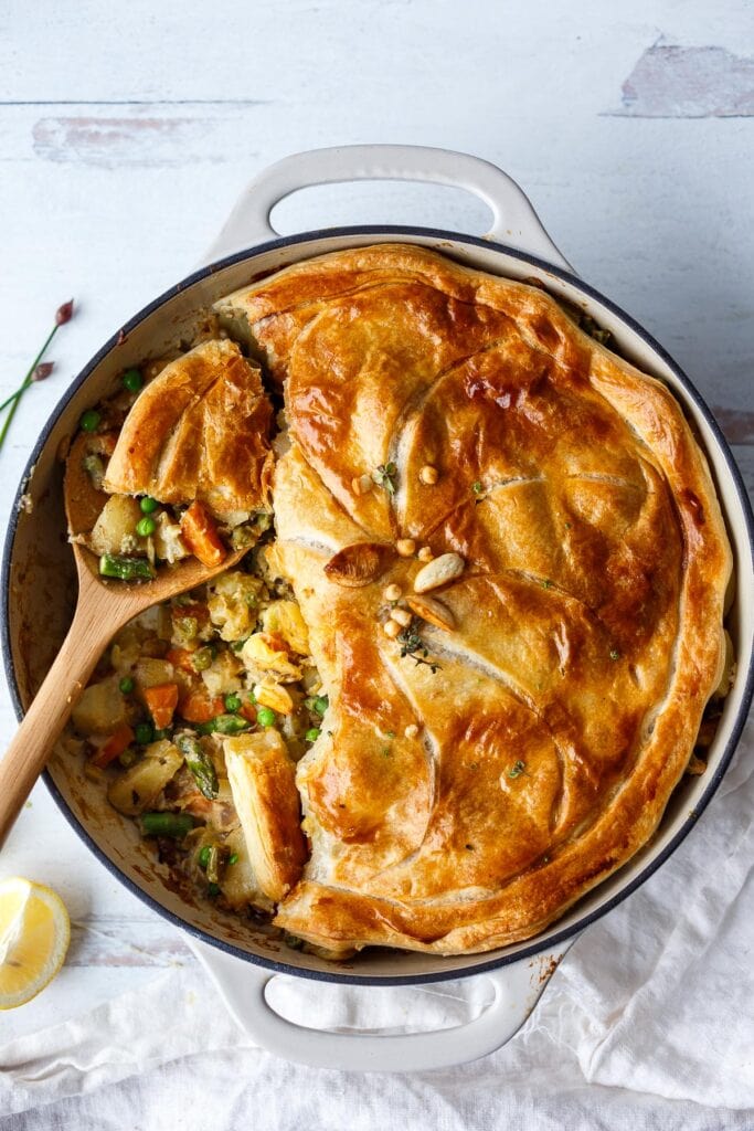 vegan pot pie with spring veggies with wood spoon lifting a scoop out, made with peas, carrots, and asparagus.