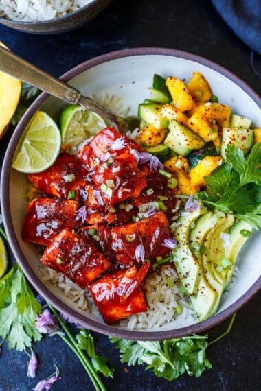 sticky gochujang salmon on rice with sliced avocado, mango cucumber salsa, and limes and cilantro, one of our adaptable recipes.