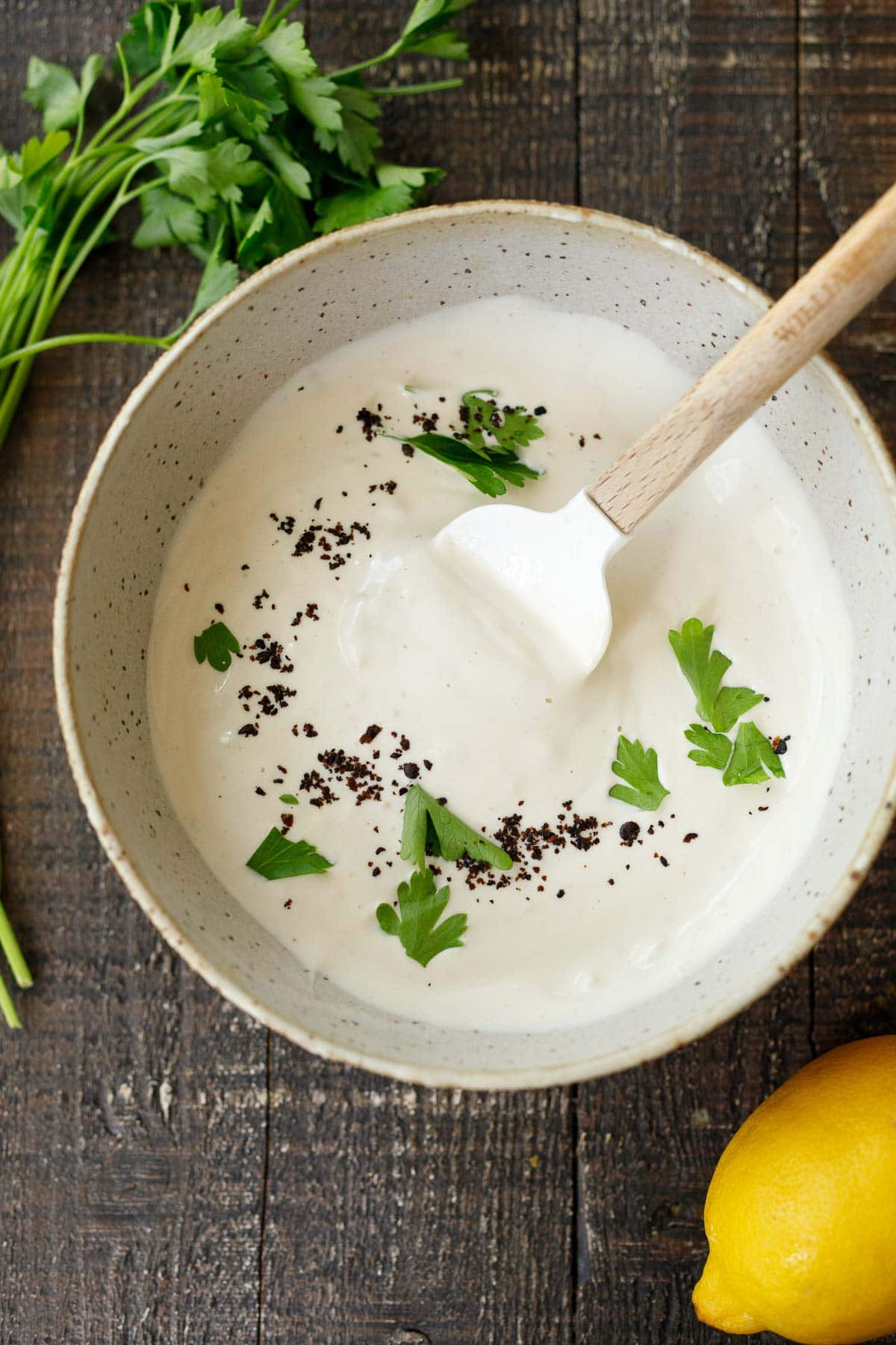 bowl with spatula and tahini yogurt sauce garnished with parsley and Aleppo chili flakes. 