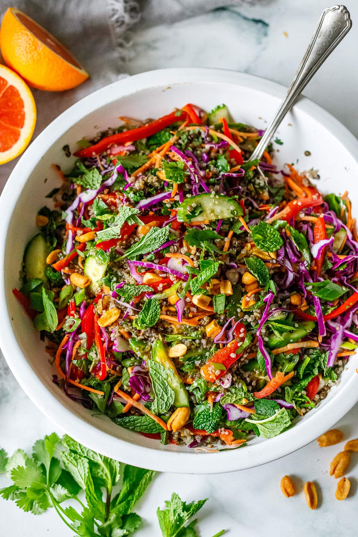 large salad bowl with thai quinoa lentil salad with shredded and sliced colorful veggies, herbs, and peanuts. 