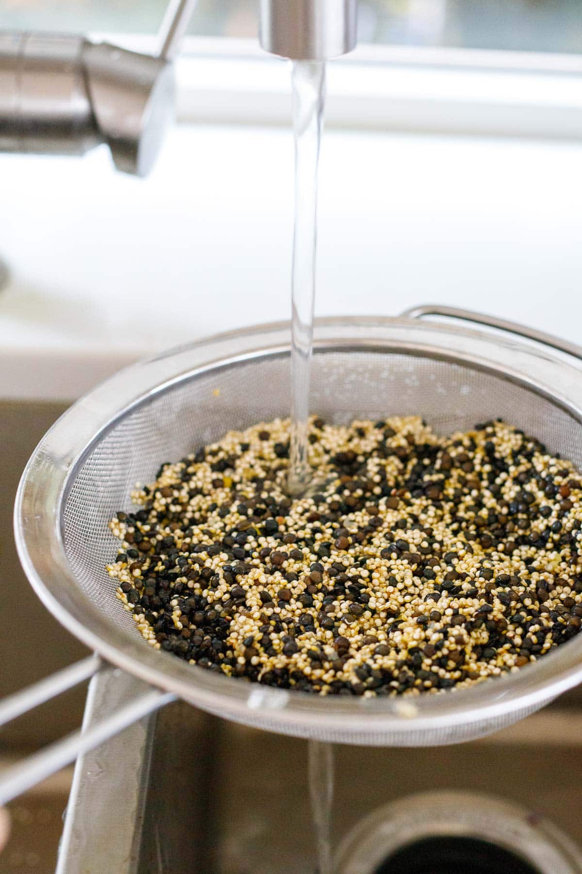 rinsing lentils and quinoa under sink with fine mesh strainer.