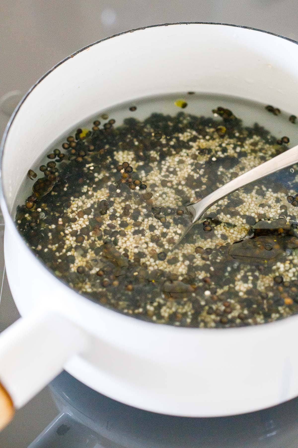 pot with lentils, quinoa, and water, and a spoon to mix.