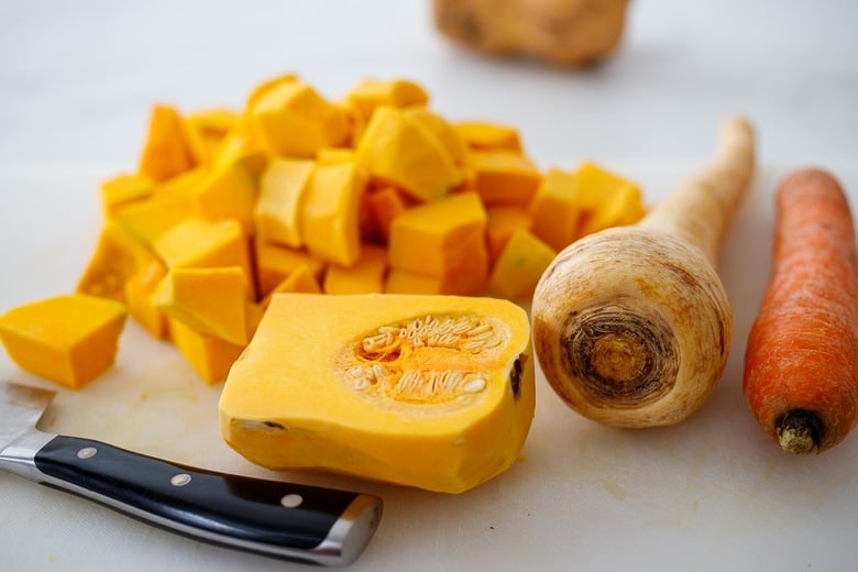 knife and cutting board with cubed butternut squash next to parsnip and carrot. 
