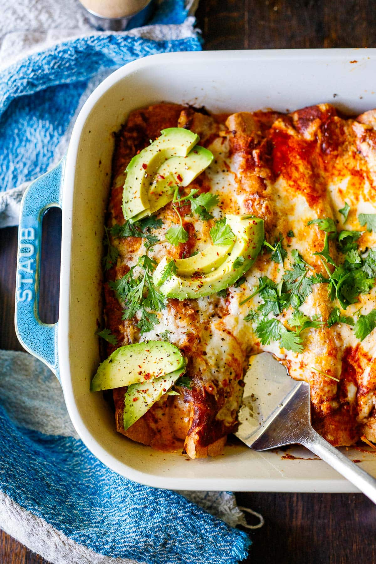 vegetable and black bean enchiladas in a blue baking dish with avocado and cilantro.