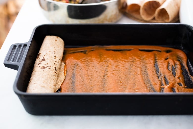 placing the rolled enchiladas in a baking dish lathered with enchilada sauce. 