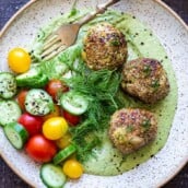 zaatar meatballs on a plate with green tahini sauce and cucumber tomato salad with fresh dill.
