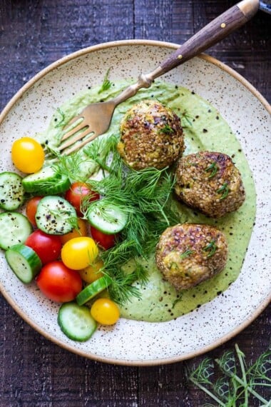 zaatar meatballs on a plate with green tahini sauce and cucumber tomato salad with fresh dill.